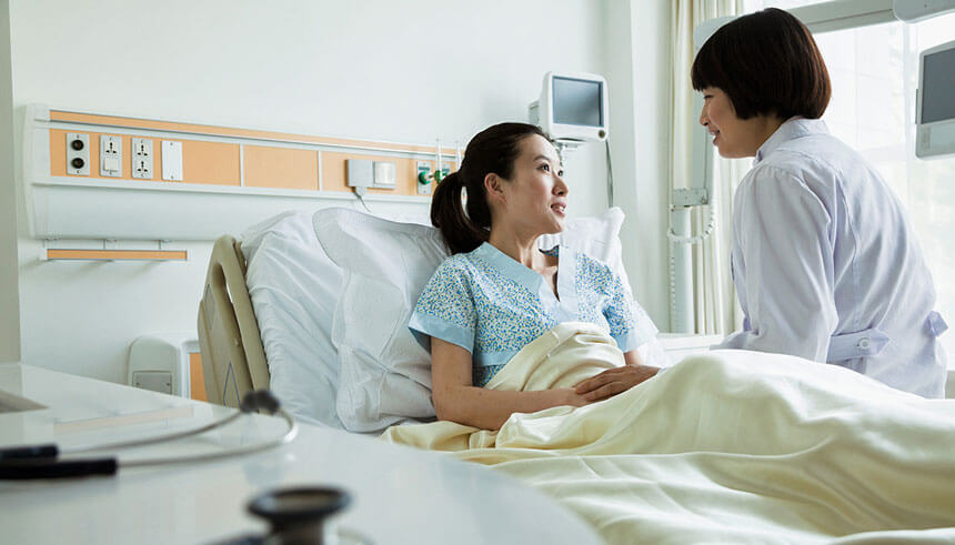 Female doctor sitting on hospital bed with patient in China