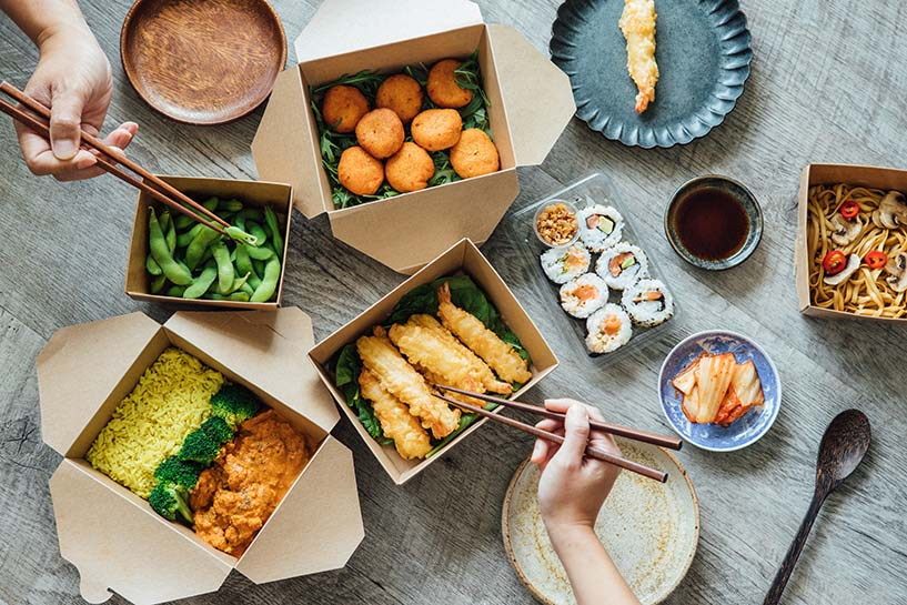 Several people eat from multiple take-out boxes of fish, sushi, and noodles.