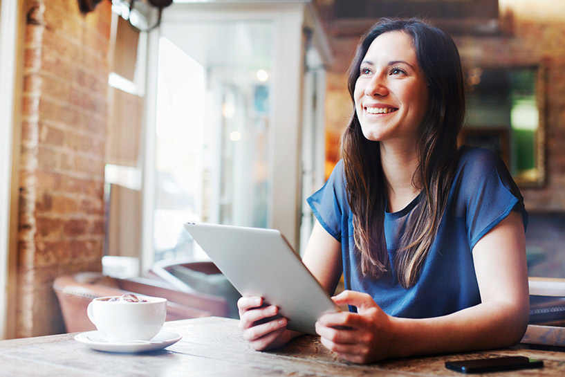 Una mujer en un café sonríe mientras usa su tableta.