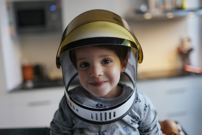 A small child wearing a toy astronaut helmet smiles.