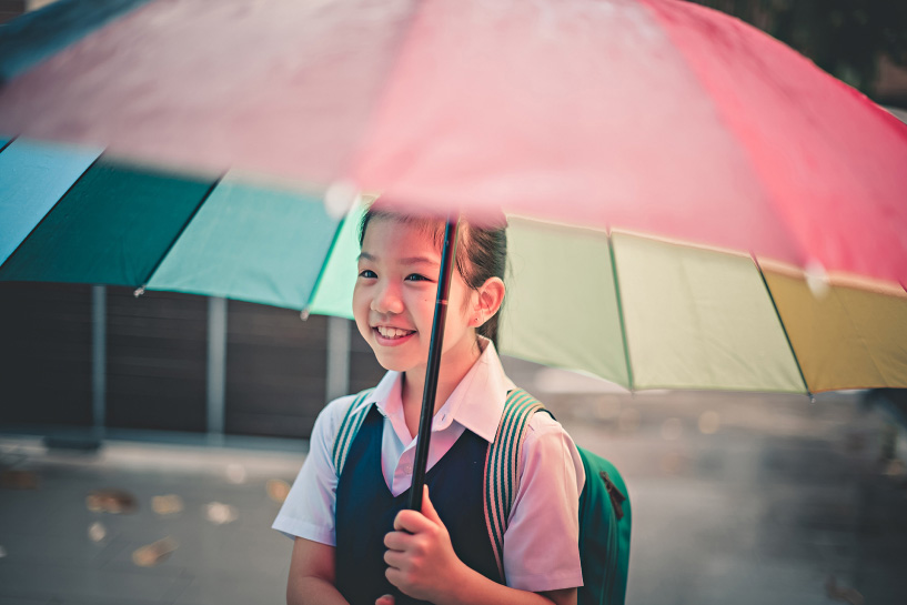 A young girl smiles as she holds a multi-colored umbrella.