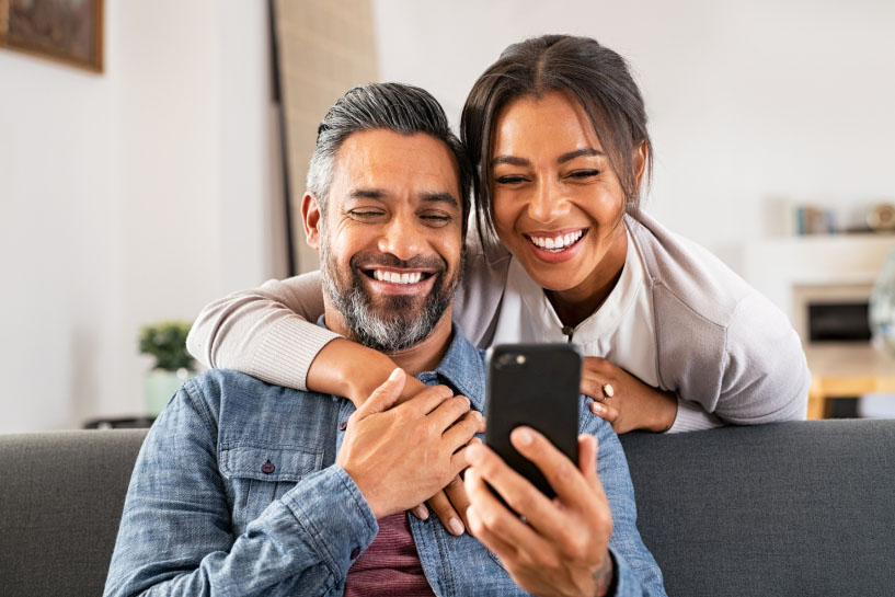 Dos personas sonrientes miran la pantalla de un teléfono móvil.
