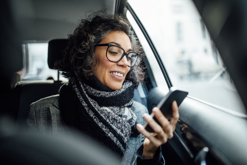 Una mujer que viaja en un automóvil sonríe mientras mira su celular.