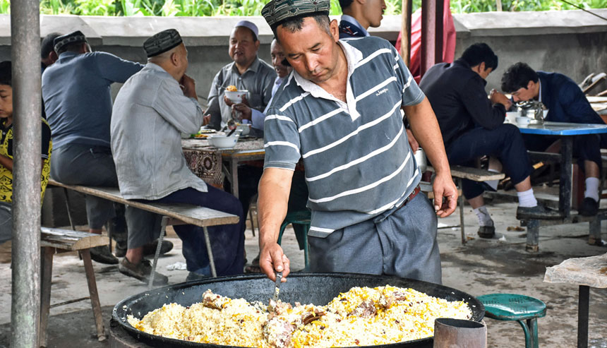 A man cooking lamb rice pilaf in a large pan outdoors