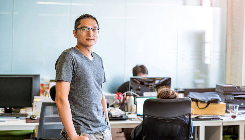 Young Asian businessman standing at his workstation in a tech start-up office