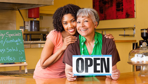 Mother and daugther, two business owners in cafe, holding open sign
