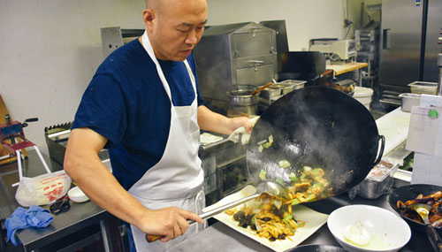 Joe Tao pours Shanxi fried pork on a plate from a wok 