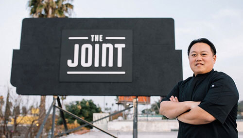 Liwei Liao, the founder of The Joint, standing in front of the restaurant billboard
