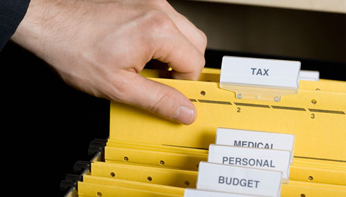 A hand picking up a file with a label Taxes on it