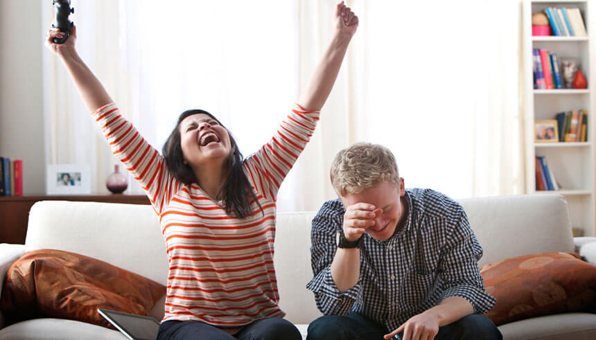 Cheering woman defeating boyfriend at video games on sofa