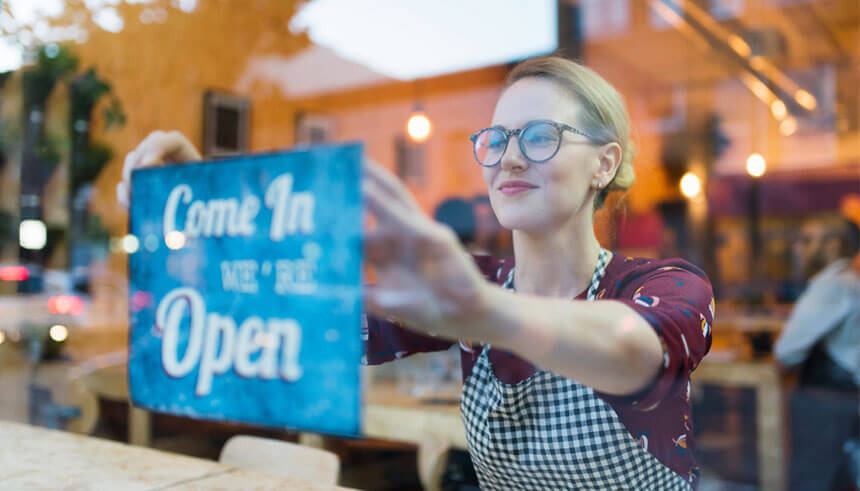 一位女性企業主在小型商業署貸款的幫助下成功創辦了自己的企業，並在店鋪窗戶上掛起「正在營業」的標識