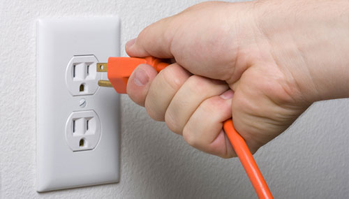 A hand unplugging an orange cord from a white outlet