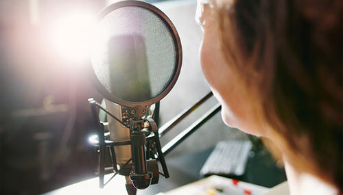 Woman speaking into a microphone in a recording studio during while doing a podcast