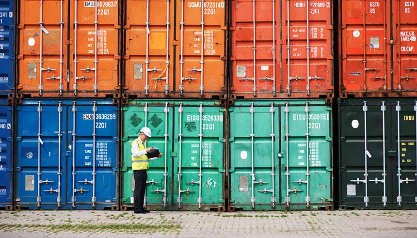 A customs inspector standing and reviewing a tack of containers