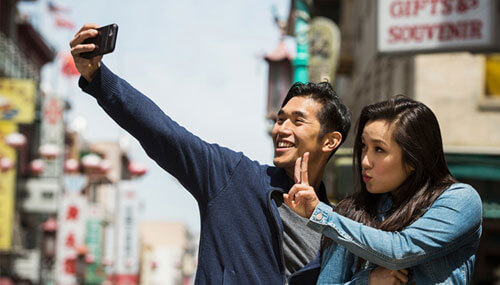Two smiling Chinese millennials posing for cell phone selfie