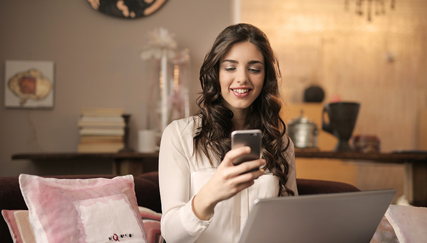 female in a room smiling while looking at her smartphone